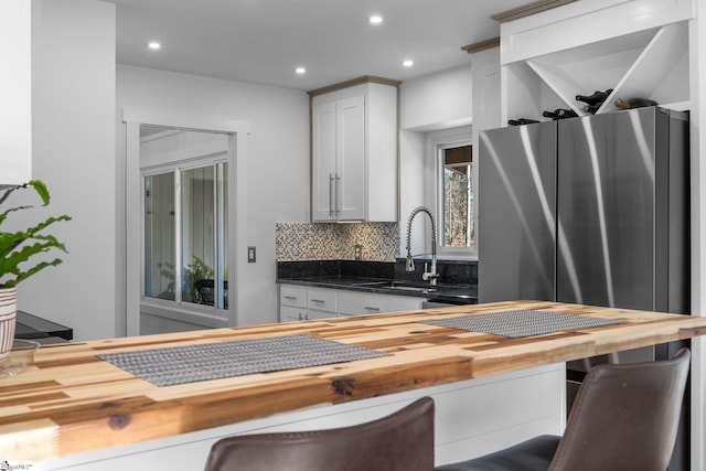 kitchen with white cabinets, a kitchen bar, backsplash, and butcher block countertops