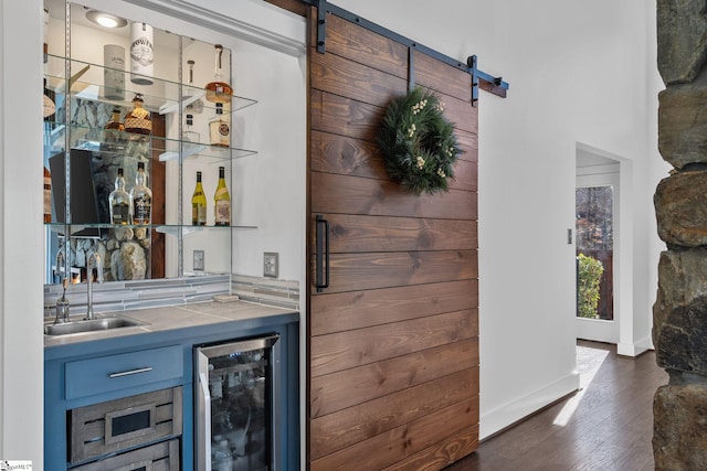 bar with tile countertops, sink, dark hardwood / wood-style floors, a barn door, and beverage cooler