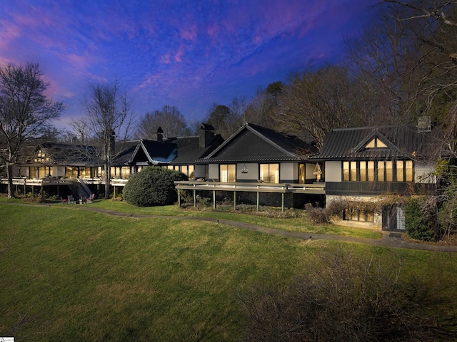 back house at dusk featuring a lawn