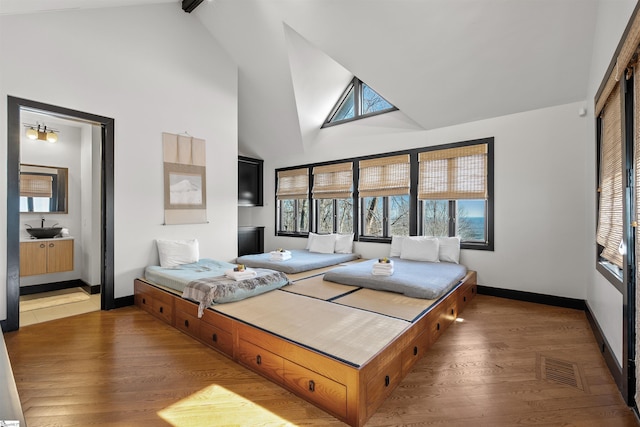 bedroom with multiple windows, ensuite bathroom, hardwood / wood-style floors, and high vaulted ceiling