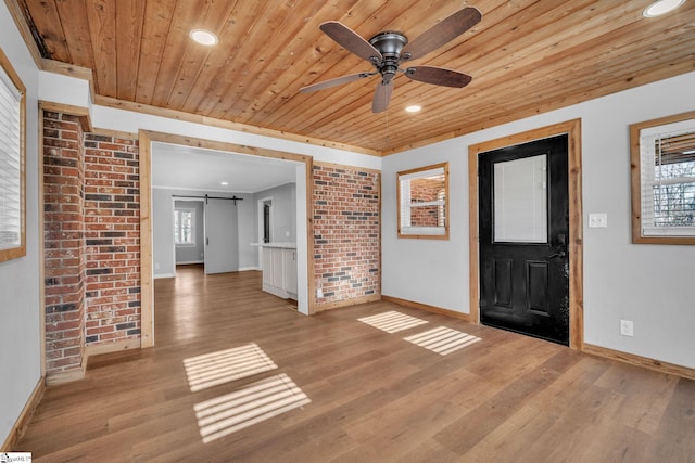 foyer entrance with brick wall, ceiling fan, a barn door, wooden ceiling, and light hardwood / wood-style floors