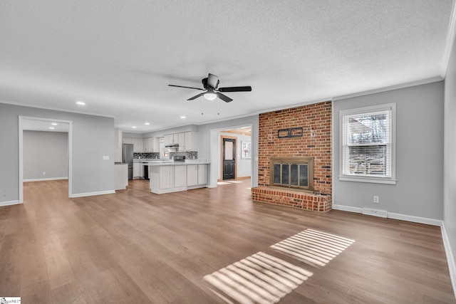 unfurnished living room featuring a fireplace, a textured ceiling, ceiling fan, and crown molding