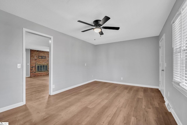 spare room with a fireplace, a wealth of natural light, light hardwood / wood-style flooring, and ceiling fan