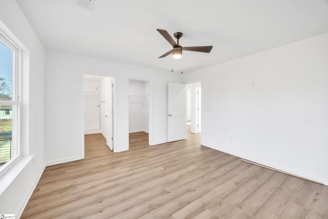 unfurnished bedroom with a closet, a spacious closet, ceiling fan, and light hardwood / wood-style flooring