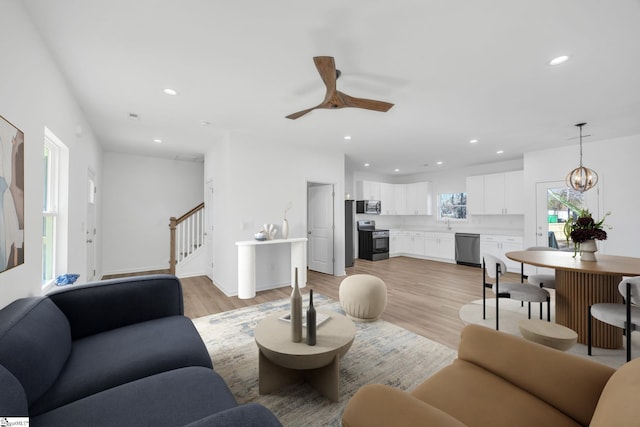 living room featuring ceiling fan with notable chandelier and light wood-type flooring