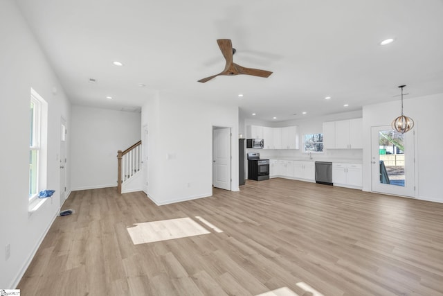 unfurnished living room with light wood-type flooring and ceiling fan with notable chandelier