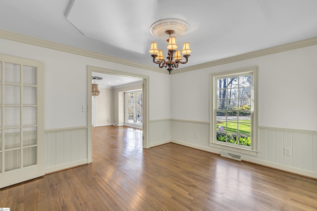 empty room featuring hardwood / wood-style flooring, ornamental molding, and an inviting chandelier