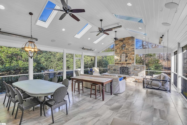 sunroom featuring an outdoor stone fireplace, ceiling fan, wooden ceiling, and lofted ceiling with skylight