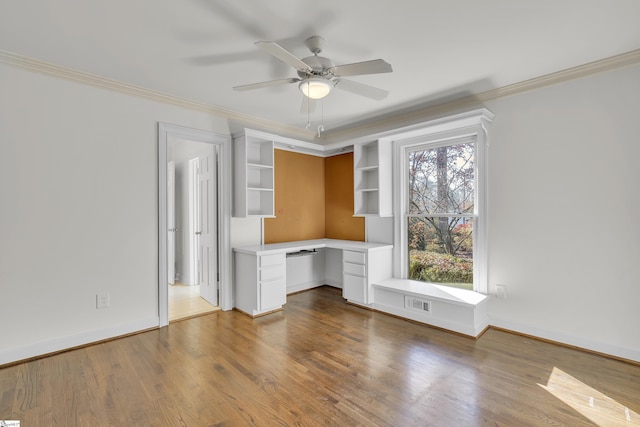 unfurnished office with hardwood / wood-style floors, ceiling fan, built in desk, and crown molding