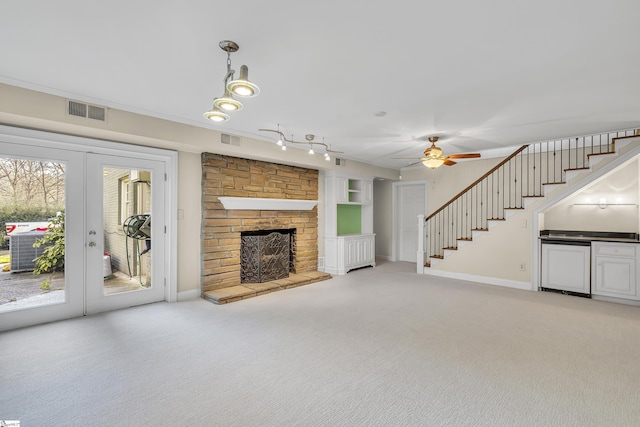 unfurnished living room with plenty of natural light, a stone fireplace, light colored carpet, and french doors