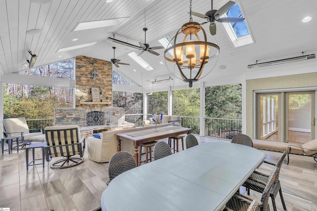 dining area with a skylight, wood ceiling, an outdoor stone fireplace, ceiling fan with notable chandelier, and high vaulted ceiling