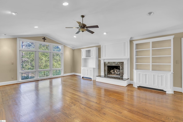 unfurnished living room with ceiling fan, built in features, a high end fireplace, crown molding, and light hardwood / wood-style floors