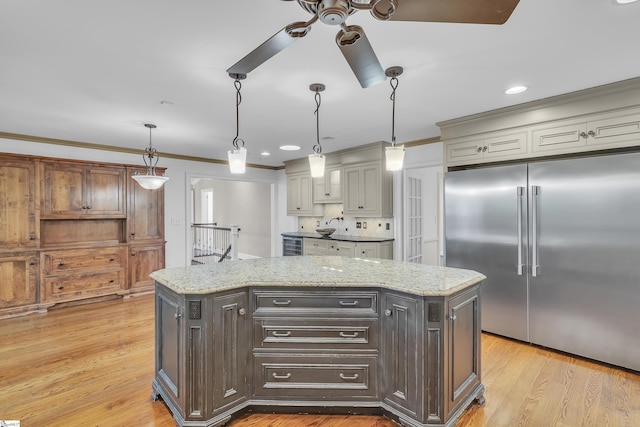 kitchen with ornamental molding, ceiling fan, decorative light fixtures, a center island, and built in refrigerator