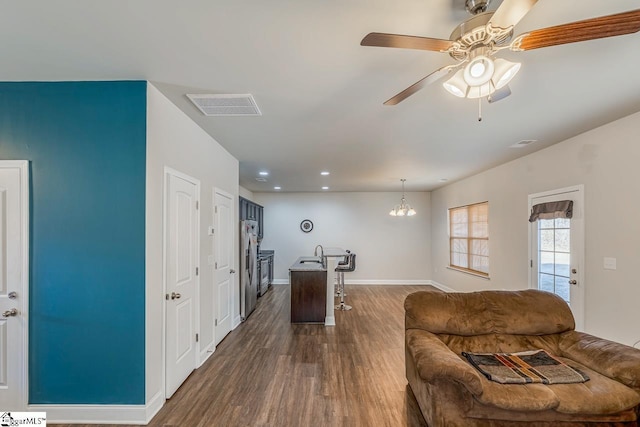 living room with ceiling fan with notable chandelier, dark wood-type flooring, and sink