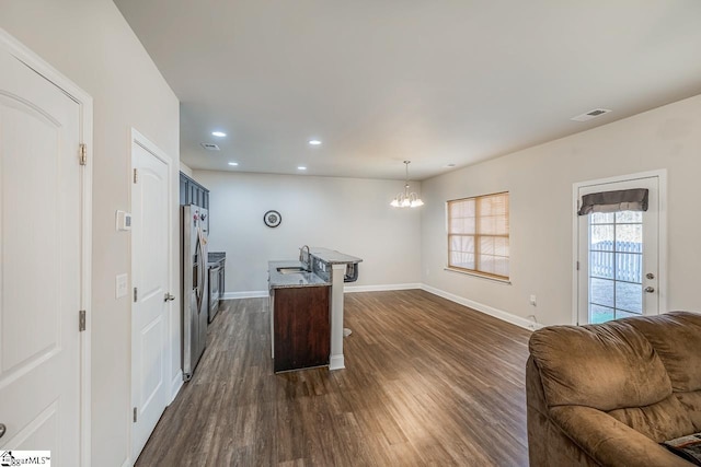 kitchen with pendant lighting, a kitchen island with sink, dark wood-type flooring, an inviting chandelier, and stainless steel refrigerator with ice dispenser