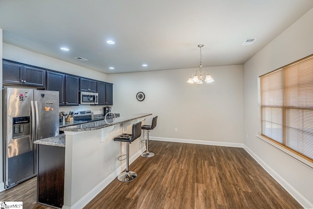 kitchen with decorative light fixtures, light stone countertops, a notable chandelier, a kitchen bar, and stainless steel appliances