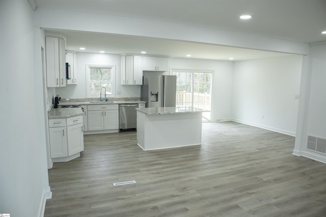 kitchen with appliances with stainless steel finishes, light wood-type flooring, sink, a center island, and white cabinetry