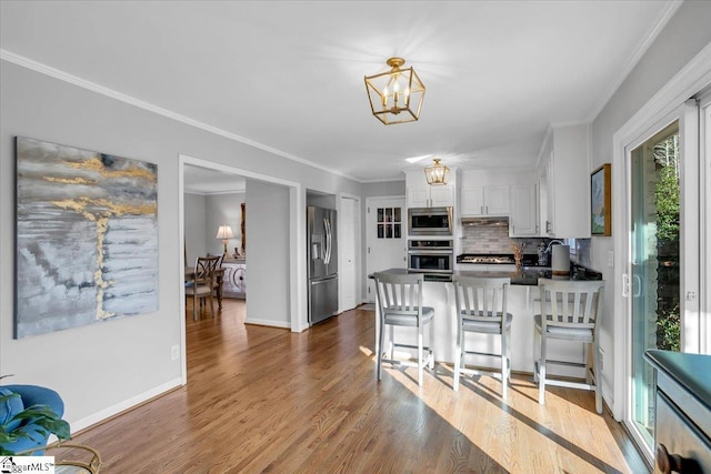 kitchen with kitchen peninsula, backsplash, a breakfast bar, stainless steel appliances, and white cabinetry