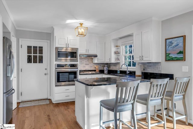 kitchen with kitchen peninsula, appliances with stainless steel finishes, backsplash, sink, and white cabinetry