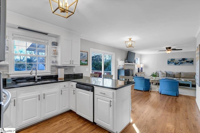 kitchen with white dishwasher, ceiling fan with notable chandelier, sink, kitchen peninsula, and white cabinetry