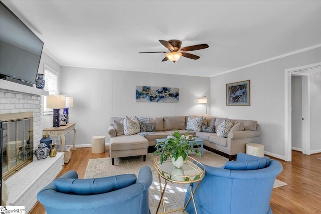 living room with crown molding, a fireplace, ceiling fan, and light wood-type flooring