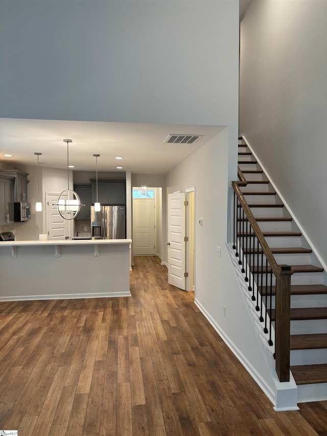 kitchen featuring kitchen peninsula, appliances with stainless steel finishes, dark wood-type flooring, an inviting chandelier, and a breakfast bar area