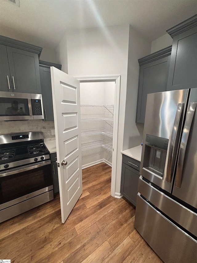 kitchen featuring appliances with stainless steel finishes, light wood-type flooring, gray cabinets, and backsplash