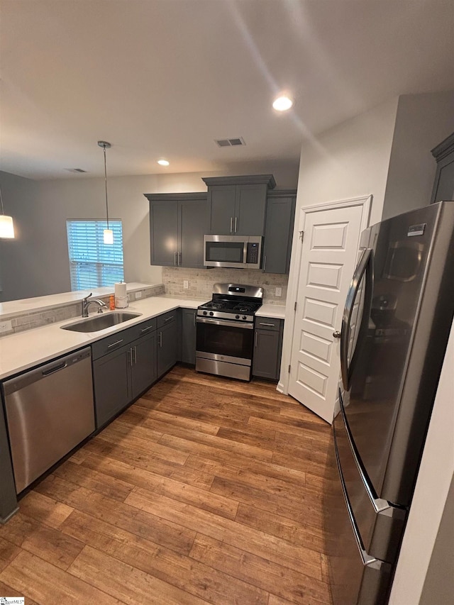 kitchen with hardwood / wood-style floors, backsplash, sink, hanging light fixtures, and stainless steel appliances