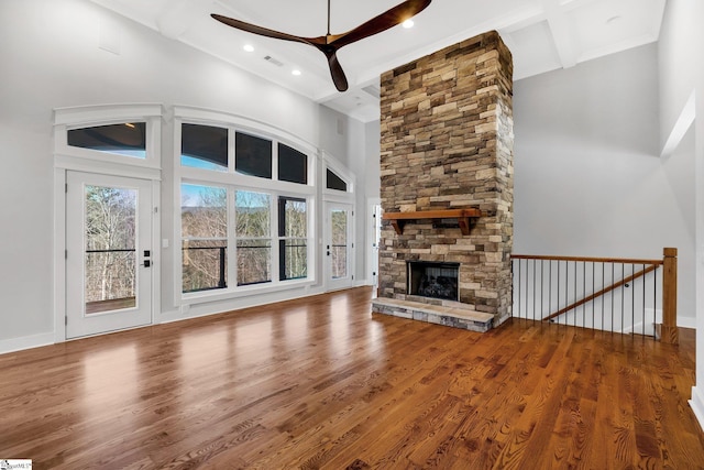 unfurnished living room featuring hardwood / wood-style flooring, ceiling fan, a towering ceiling, a fireplace, and beam ceiling