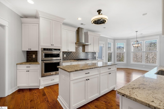 kitchen with a center island, wall chimney exhaust hood, light stone countertops, white cabinetry, and stainless steel appliances