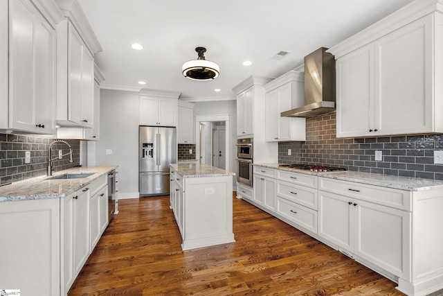 kitchen with white cabinets, a center island, stainless steel appliances, and wall chimney range hood