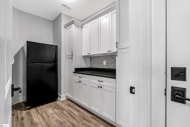 kitchen featuring tasteful backsplash, white cabinetry, black refrigerator, and light hardwood / wood-style floors