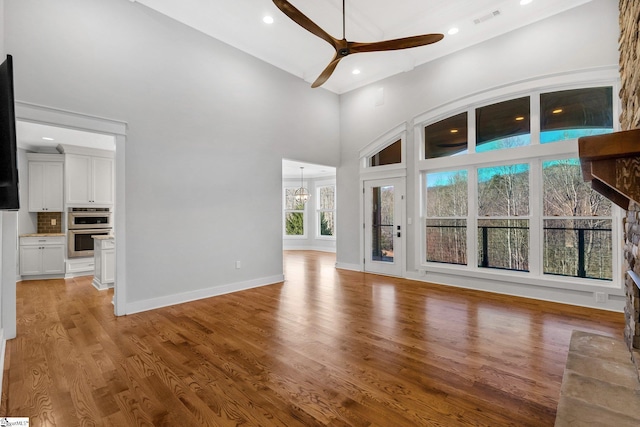 unfurnished living room featuring ceiling fan, light hardwood / wood-style floors, and a high ceiling