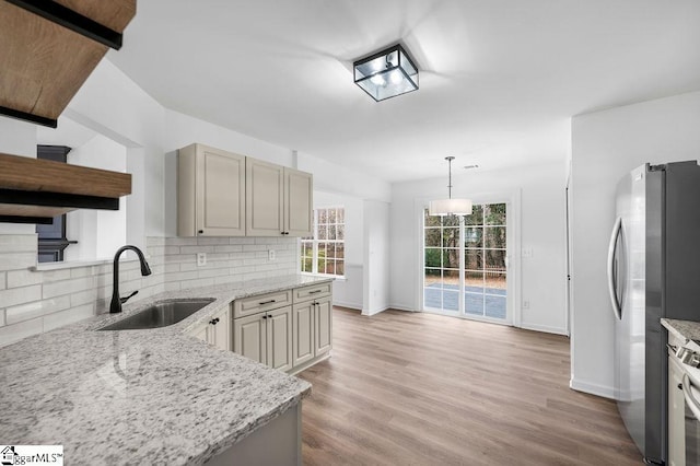 kitchen with light stone countertops, tasteful backsplash, sink, stainless steel refrigerator, and hanging light fixtures