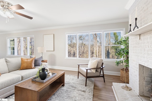 living room with ceiling fan, wood-type flooring, crown molding, and a brick fireplace