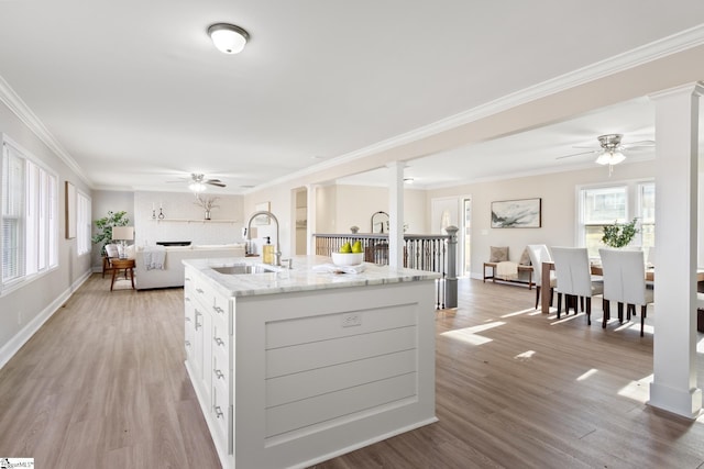 kitchen featuring white cabinets, a center island with sink, ornamental molding, and sink