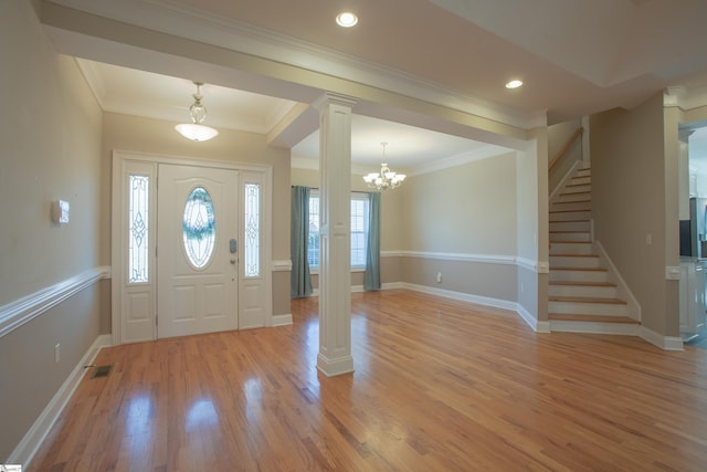 foyer entrance featuring ornate columns, ornamental molding, light hardwood / wood-style floors, and a notable chandelier