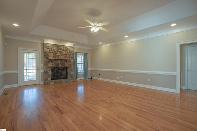 unfurnished living room with ceiling fan, a healthy amount of sunlight, a fireplace, and a tray ceiling