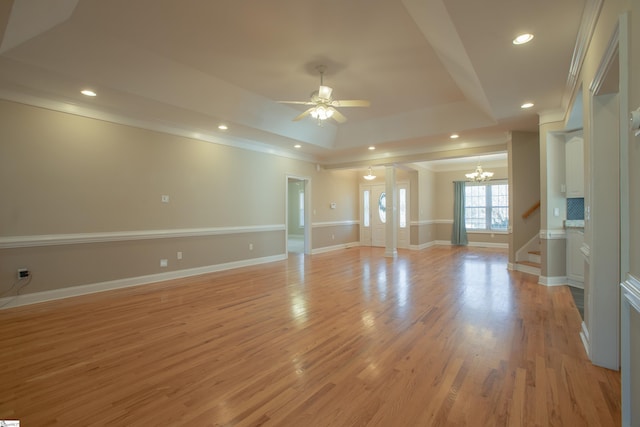 unfurnished living room featuring ceiling fan with notable chandelier, a raised ceiling, crown molding, and light hardwood / wood-style flooring