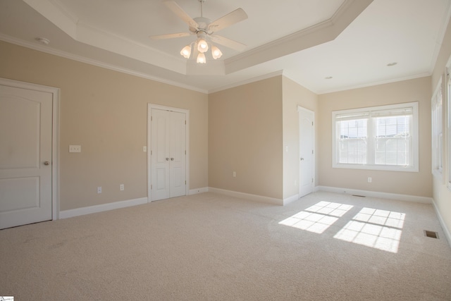 unfurnished room with light colored carpet, ceiling fan, a raised ceiling, and ornamental molding