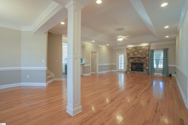 unfurnished living room featuring light wood-type flooring, decorative columns, a tray ceiling, ceiling fan, and a fireplace