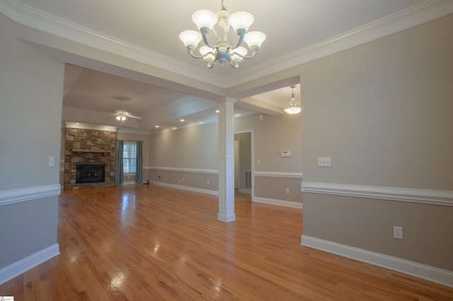 unfurnished living room featuring decorative columns, ceiling fan with notable chandelier, crown molding, light hardwood / wood-style floors, and a stone fireplace