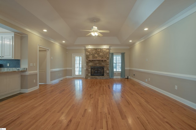 unfurnished living room featuring a raised ceiling, ceiling fan, a fireplace, and light hardwood / wood-style floors