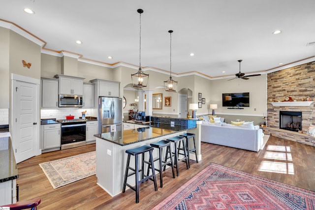 kitchen featuring ceiling fan, hardwood / wood-style floors, decorative light fixtures, a kitchen bar, and appliances with stainless steel finishes