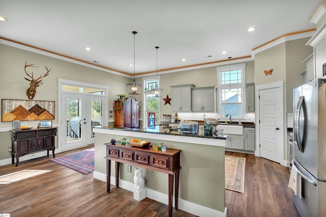 kitchen featuring stainless steel refrigerator, hanging light fixtures, a kitchen breakfast bar, gray cabinets, and ornamental molding