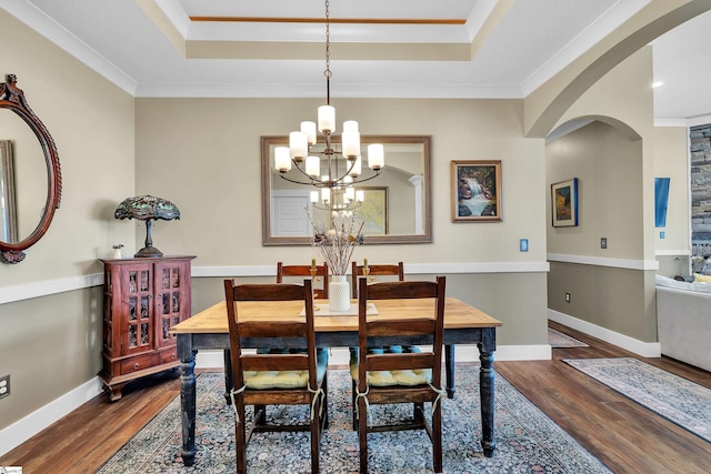 dining room featuring a raised ceiling, crown molding, dark wood-type flooring, and a notable chandelier