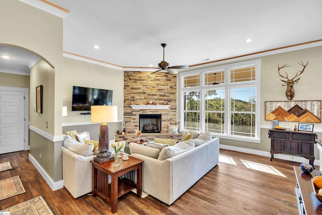 living room featuring a stone fireplace, crown molding, ceiling fan, and wood-type flooring