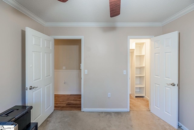 unfurnished bedroom featuring a walk in closet, light carpet, a textured ceiling, and ornamental molding