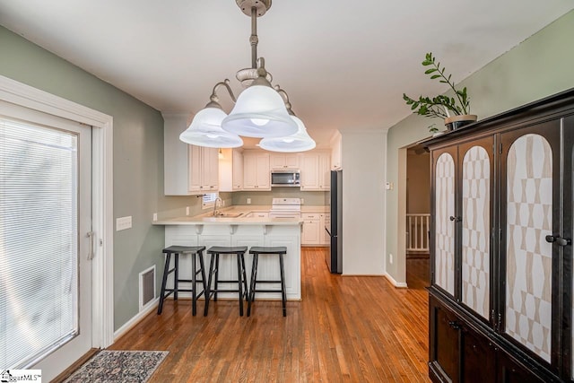 kitchen featuring sink, hanging light fixtures, kitchen peninsula, a kitchen bar, and appliances with stainless steel finishes