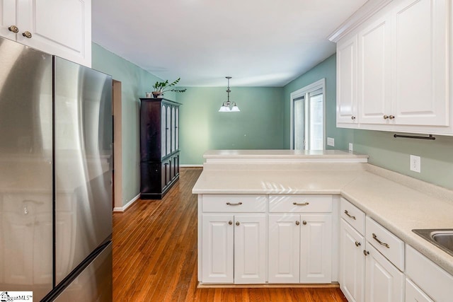 kitchen featuring hardwood / wood-style floors, white cabinetry, stainless steel refrigerator, and hanging light fixtures